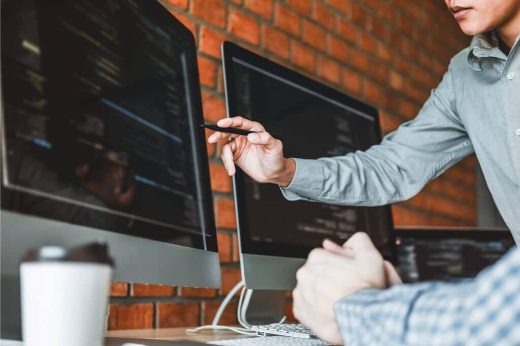 na foto, um homem apontando para a tela do computador e mostrando informações em códigos tecnológicos