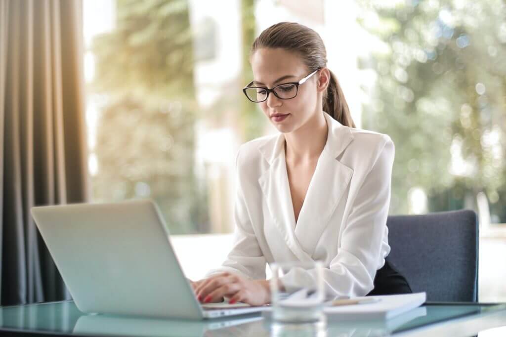 Imagem de uma mulher sentada em sua mesa de trabalho digitando no computador.